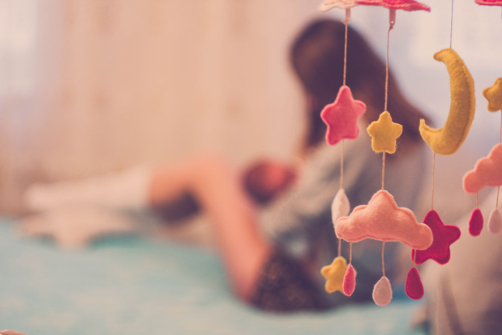 Woman breastfeeding, blurred background with baby mobile in foreground